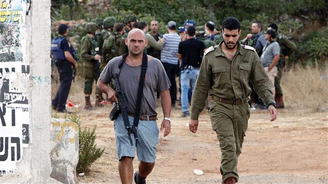 An armed Israeli settler and a member of the Israeli forces walk on a road in the occupied southern West Bank at the entrance of the Kiryat Arba settlement on September 23, 2016. (Photo by AFP)