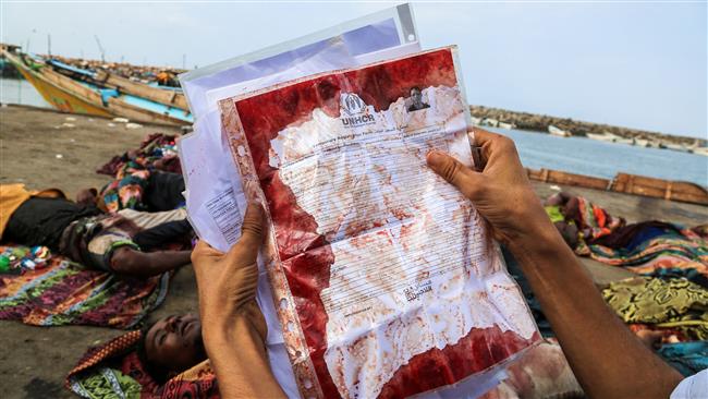 A picture taken on March 17, 2017, shows a man holding temporary registration form for refugees with the UNHCR, covered in blood, of one of the persons killed in a boat carrying Somali refugees, in front of the dead bodies arriving at Yemen