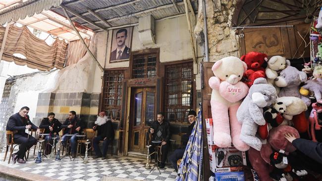 Syrians sit outside a cafe bearing the image of President Bashar al-Assad in the old part of the capital Damascus on February 12, 2017. (Photo by AFP)
