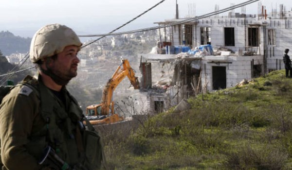Israeli soldier stands in front of illegal Israeli settlement units