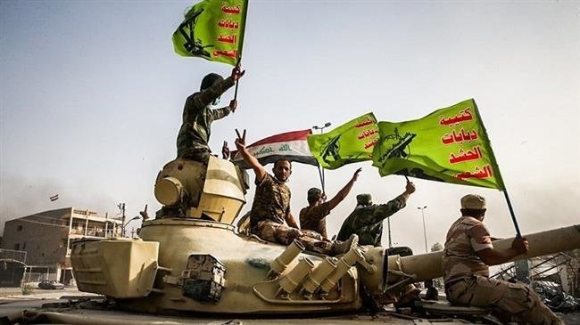 In this file picture, Iraqi pro-government fighters from Popular Mobilization Units (better known by the Arabic word Hashd al-Sha’abi) raise the national Iraqi and Popular Mobilization Forces flags as they celebrate the ouster of Daesh Takfiri terrorist group from Fallujah.
