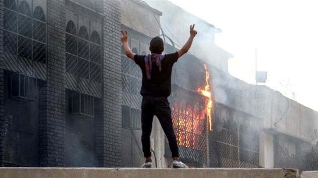 An Iraqi protester stands on the ledge of a wall watching the burning of the Basra airport