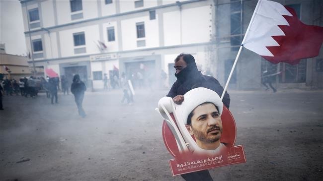 In this file photo, taken on February 13, 2015, a Bahraini protester carrying a placard showing Sheikh Ali Salman — a prominent Shia cleric — takes cover from tear gas during clashes with police following a demonstration against Salman’s detention. (By AFP)
