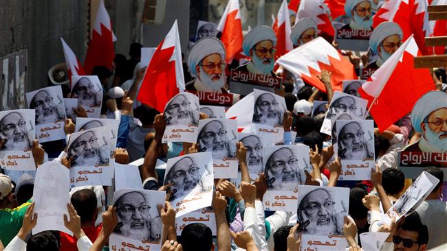 People holding Bahraini flags and placards with images of top Shia cleric, Sheikh Isa Qassim, shout slogans during an anti-regime protest after the Friday prayers in Diraz, west of Manama, Bahrain