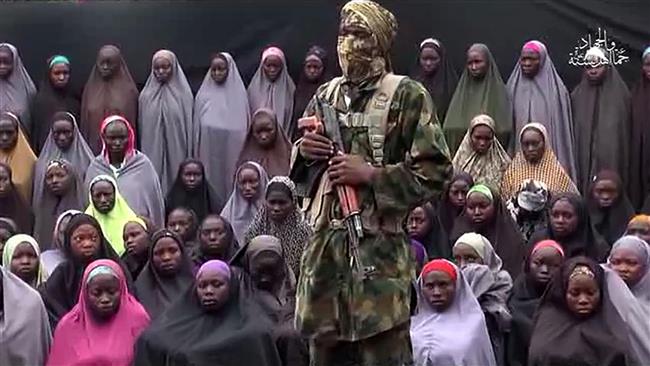 This video grab image created on August 14, 2016, taken from a video released on YouTube purportedly by the Boko Haram Takfiri terrorist group shows what is claimed to be one of the group’s militants at an undisclosed location standing in front of girls kidnapped from Chibok, Nigeria, in April 2014. (Via AFP)
