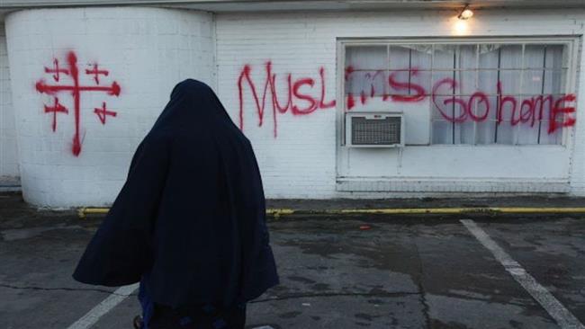 A Muslim woman seen walking past a wall spray-painted, "Muslims go home" 