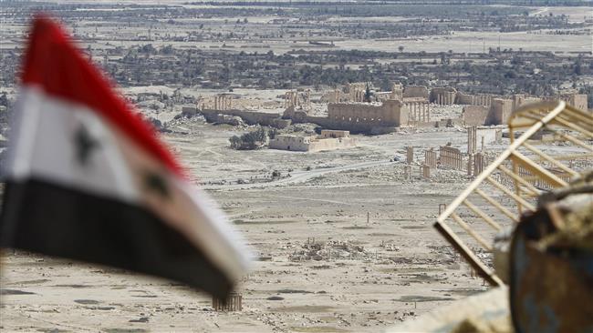 A Syrian national flag flutters as the ruins of the historic city of Palmyra are seen in the background, in Homs Governorate, Syria