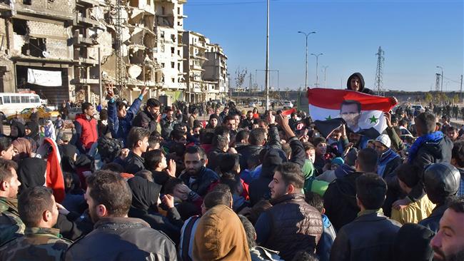 A man holds the Syrian flag bearing a portrait of the Syrian president as residents in a government-held area of Aleppo on December 15, 2016. (Photo by AFP)
