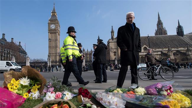 A police officer walks by floral tributes with other bystanders in Parliament Square in front of the Houses of Parliament in central London on March 24, 2017 two days after the March 22 terror attack on the British parliament and Westminster Bridge. (Photo by AFP)
