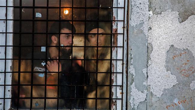 Refugees look through a barrack window in a refugee camp