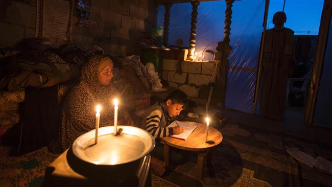 A Palestinian woman helps her son study by candlelight at their makeshift home in the Khan Yunis refugee camp in the southern Gaza Strip on April 19, 2017. (Photo by AFP)
