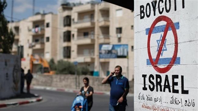 Palestinians walking past a sign painted on a wall calling to boycott Israeli products, in the West Bank town of Bethlehem