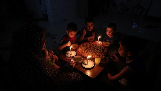 A Palestinian family eats dinner by candlelight at their makeshift home in Rafah refugee camp, in the southern Gaza Strip, during a power outage on June 11, 2017. (Photo by AFP)
