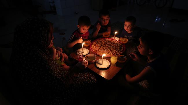 A Palestinian family eats dinner by candlelight at their makeshift home in the Rafah refugee camp, in the southern Gaza Strip, during a power outage on June 11, 2017. (Photo by AFP)
