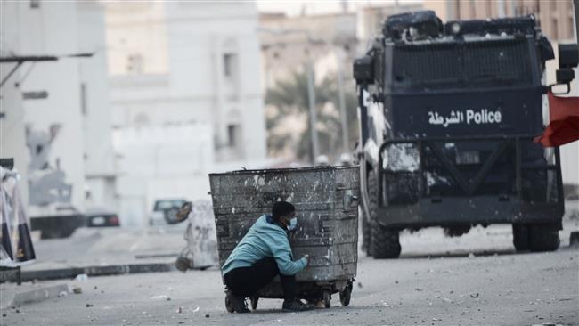 A photo taken on January 2, 2015 shows a Bahraini protester taking cover behind a garbage container during clashes with riot police in the village of Bilad al-Qadeem, on the outskirts of the capital, Manama, January 2, 2015. (By AFP)
