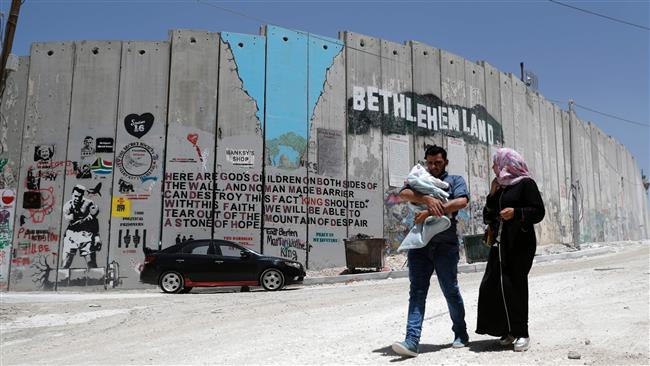 Palestinian family walk past a graffiti painted on the Israeli apartheid wall in the West Bank city of Bethlehem on May 15, 2017. (Photo by AFP)
