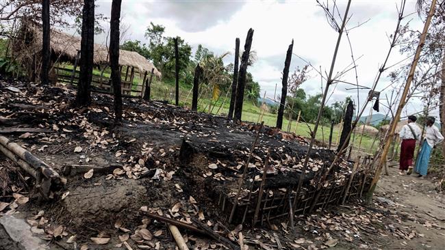 This photo taken on July 14, 2017 shows people walking near a house destroyed during clashes between security personnel and militants in Tinmay village, Buthidaung township in Myanmar