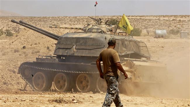 A fighter walks past a tank bearing a Hezbollah flag in the Qara area, in Syria