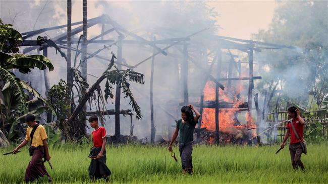 In this photograph taken on September 7, 2017, unidentified men carry knives and slingshots as they walk past a burning house in Gawdu Tharya village near Maungdaw in Rakhine state, Myanmar. (Photo by AFP)
