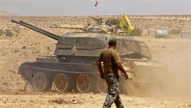 A Hezbollah fighter walks past a tank bearing a flag of the Lebanese resistance movement flag in the Qara area, in Syria