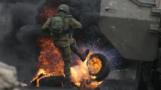 TOPSHOT - An Israeli soldier removes burning tires from the road during clashes with Palestinian protesters following a demonstration against the expropriation of Palestinian land by Israel in the village of Kfar Qaddum, near Nablus in the occupied West Bank, on September 15, 2017.  (Photo by AFP)