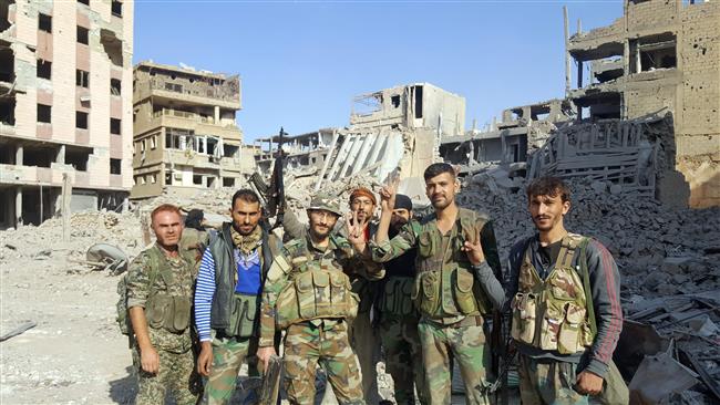 Syrian soldiers and government forces pose for a picture in front of damaged buildings in the eastern Syrian city of Dayr al-Zawr on November 3, 2017. (Photo by AFP)
