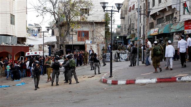 Palestinians (L) gather around an ambulance as Israeli forces (C) stand guard while Israeli settlers walk to a religious site in the city of al- Khalil Hebron in the Israeli-occupied West Bank, on November 11, 2017. (Photo by AFP)
