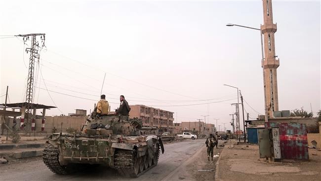 Pro-Syrian government forces ride on a tank as it drives down a street in the Syrian border town of Albu Kamal on November 20, 2017. (Photo by AFP)
