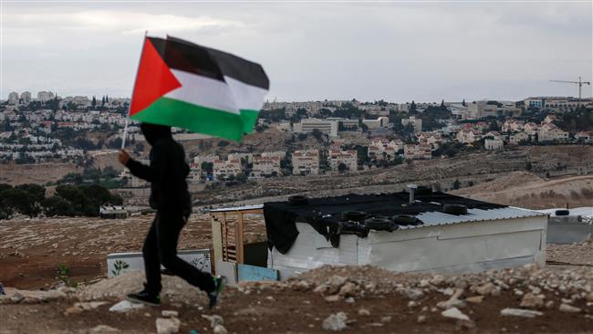 A Palestinian boy waves a national flag as he runs during a demonstration against the potential demolition of the Jabal al-Baba Bedouin encampment, near the Israeli settlement of Ma
