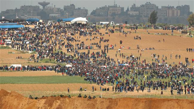 A photo taken on March 30, 2018 from across the border from the besieged Gaza Strip shows Palestinians taking part in a tent city protest marking Land Day. Israeli soldiers are seen in the foreground. (By AFP)
