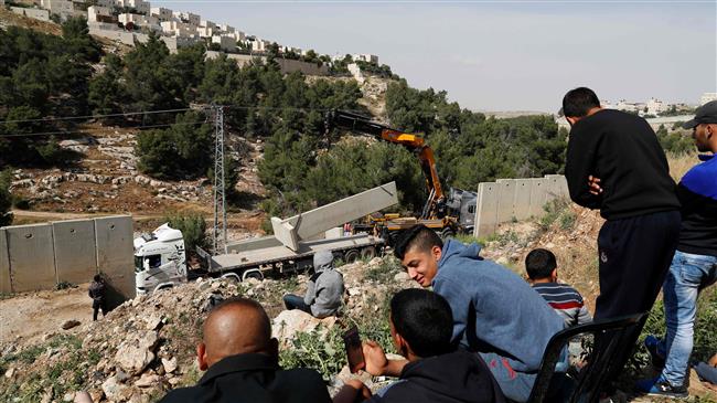 This picture taken on April 27, 2018, shows Palestinians from Shuafat refugee camp in East Jerusalem al-Quds watching as Israeli forces replace the collapsed sections of the controversial Israeli separation wall, dividing the camp from the Israeli settlement of Pisgat Zeev (L) after it collapsed the day before due to heavy rainfall and floods. (Photo by AFP)
