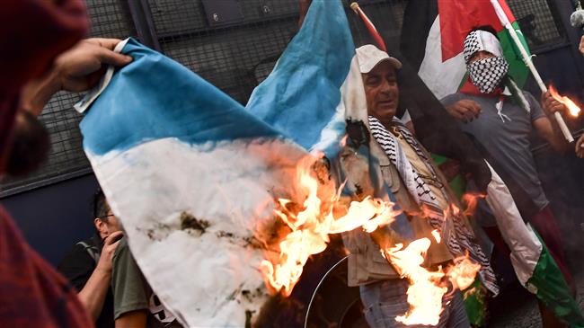 Protesters burn an Israeli flag and shout slogans in front of the embassy of the Israeli regime during a demonstration in central Athens on May 15, 2018. (AFP)
