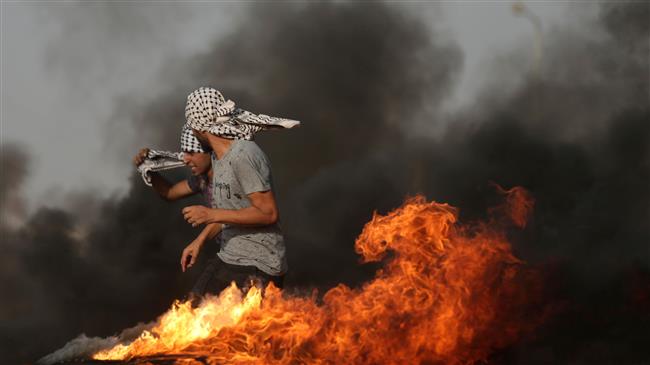 A Palestinian demonstrator walks in the smoke billowing from burning tyres during clashs with Israeli forces along the border with the Gaza Strip, on May 18, 2018. (Photo by AFP)
