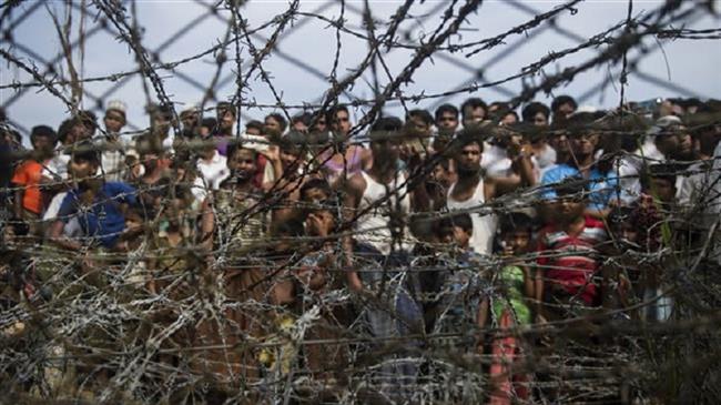 Rohingya refugees gather behind a barbed-wire fence in a temporary settlement setup in a 
