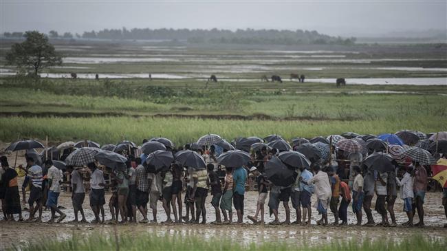 Rohingya Muslim refugees wait in line under the rain during a food distribution at Nayapara refugee camp in Bangladesh