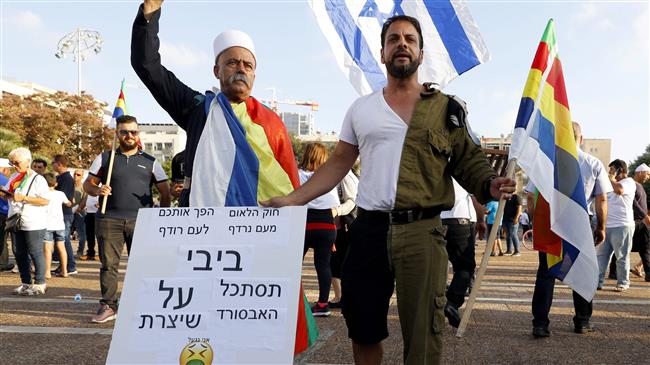 A former Israeli Druze officer (R) holds a banner that reads in Hebrew "Bibi looks at the absurdity that you have created with your law" as members of the Israeli Druze community and their supporters demonstrate to protest against the 