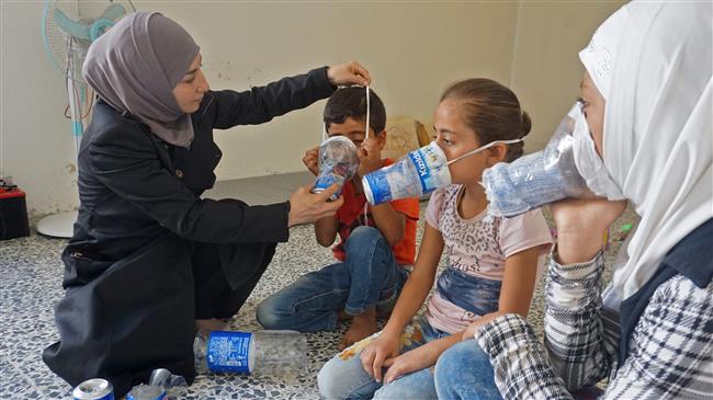 Um Majid (L) tries an improvised gas mask on family members in her home in Binnish in Syria