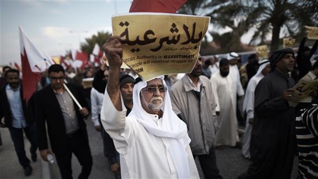 The file photo, taken on December 26, 2014, shows a Bahraini man holding up a placard reading in Arabic, "Your government and your parliament are without legitimacy," during an anti-government protest in the village of Jannusan, west of the capital Manama. (Photo by AFP)
